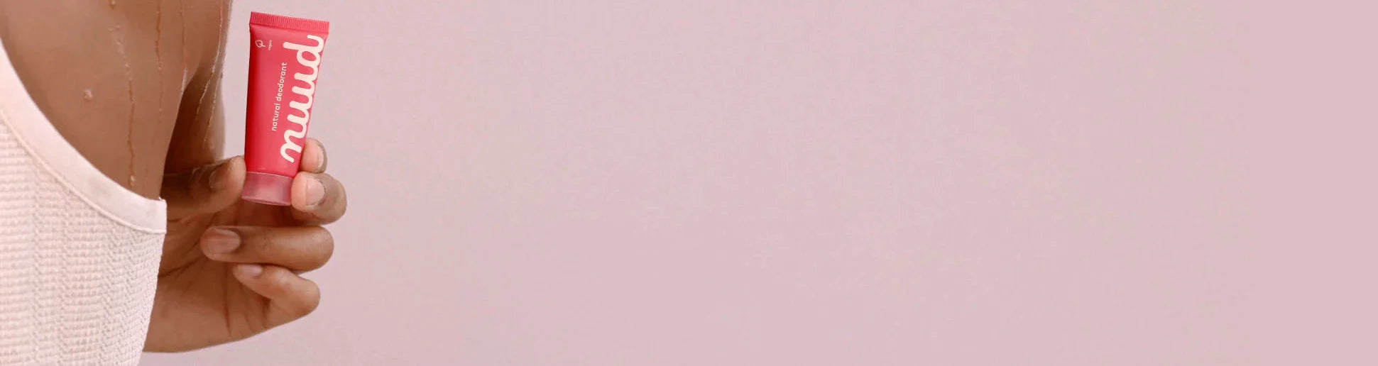 A hand holding a tube of nuud against a pink ground
