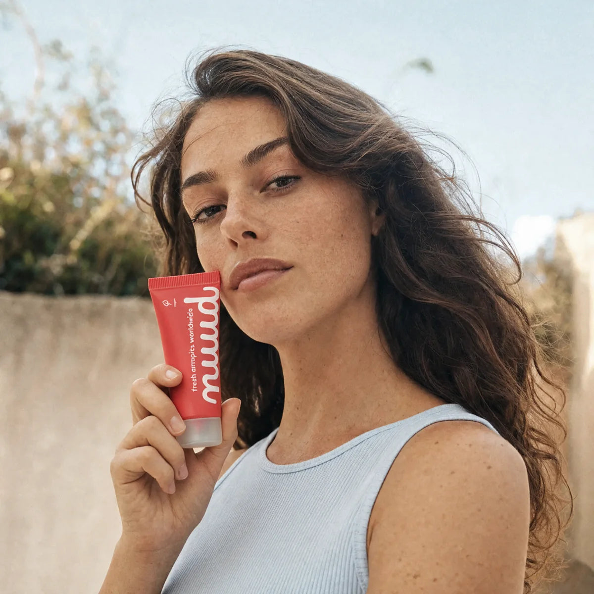 A woman holding a tube of nuud against her cheek